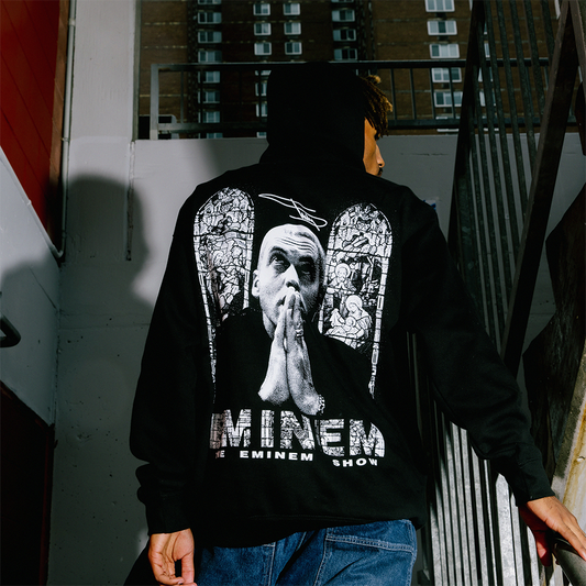 Person wearing a black hoodie with a graphic design and 'Eminem' text, standing in an urban setting.